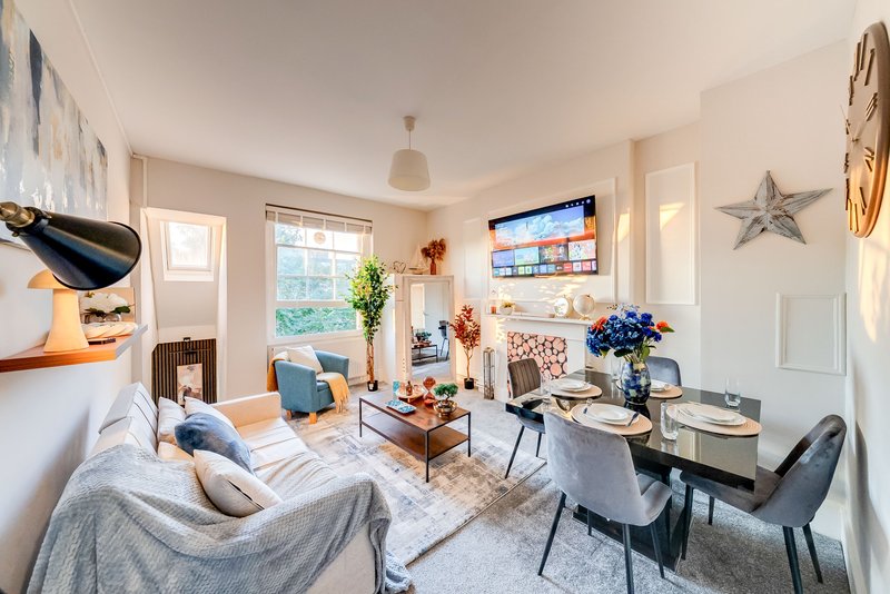 Open-plan living space with sofa, dining table, TV wall, and natural light from windows