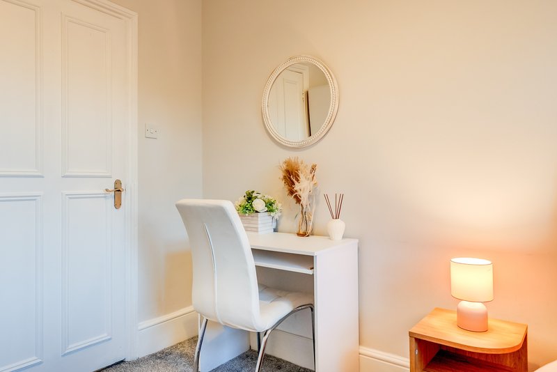 Bright bedroom corner with white desk, chair, round mirror, and bedside lamp