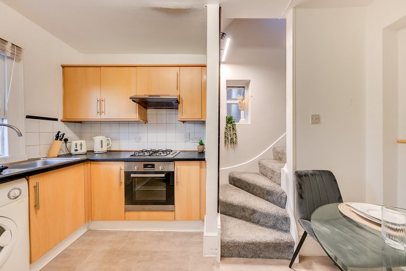 Modern kitchen with orange cabinetry, black countertop, and view into hallway with stairs