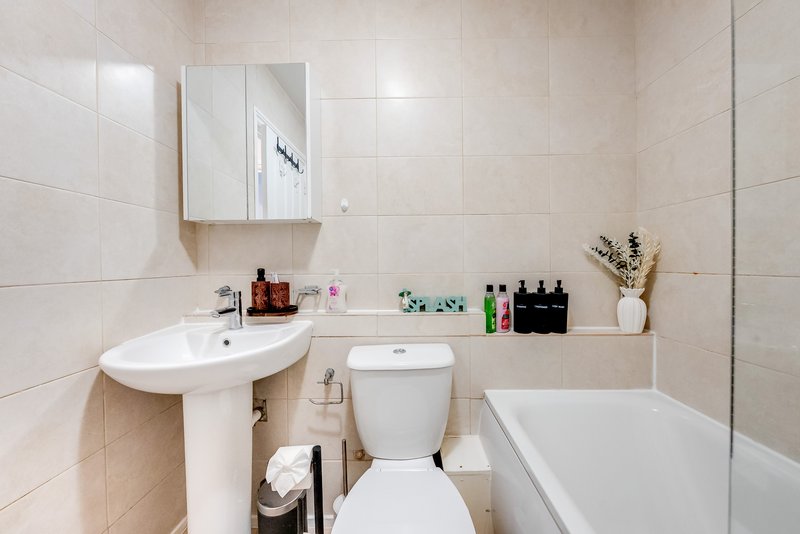 Clean bathroom with pedestal sink, toilet, bathtub, mirror cabinet and shelving with toiletries