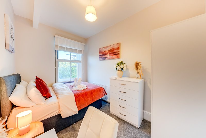 Bright bedroom with single bed, white dresser, window and warm lighting
