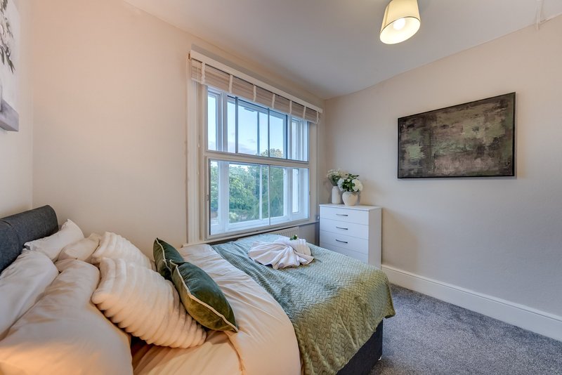 Bright bedroom with double bed, white dresser, large window and framed artwork on wall