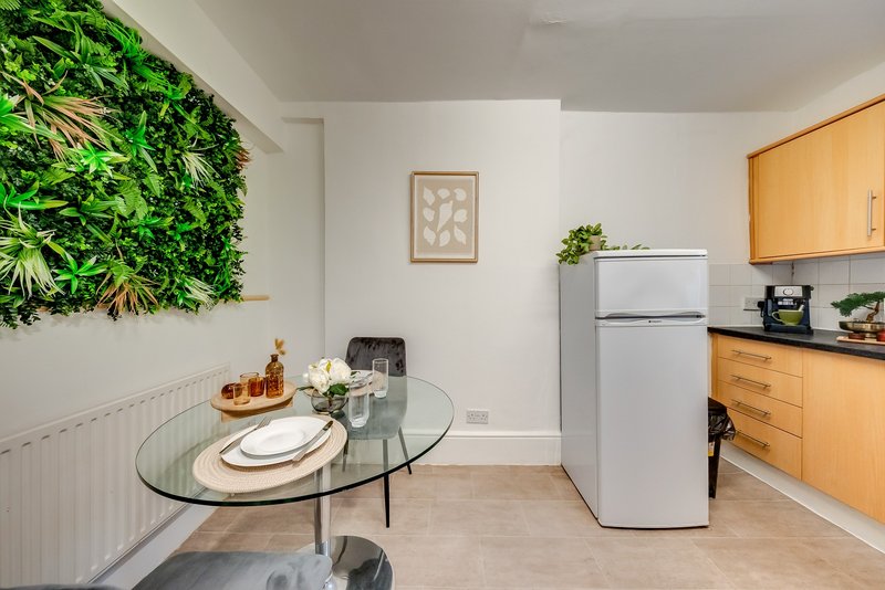 Modern kitchen with wooden cabinets, white fridge, dining table and green wall plant