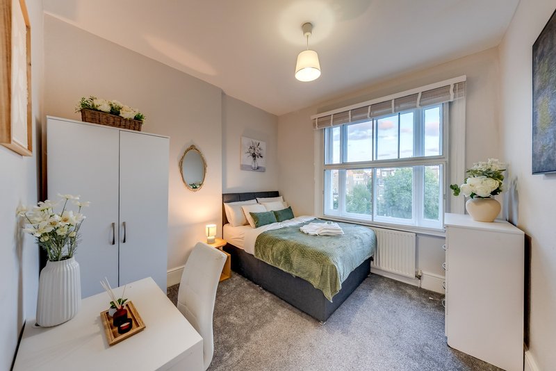 Bright bedroom with double bed, white wardrobes, desk, and large bay window