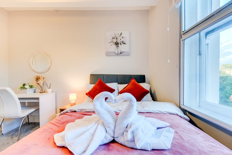 Bright modern bedroom with double bed, decorative towel swans, red cushions and large windows