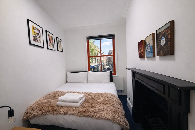 Small bedroom with double bed, brown fur throw, framed wall art, window and fireplace