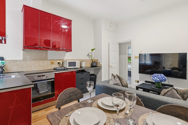 Open-plan kitchen and living room with red cabinets, dining table set for two, and wall-mounted television