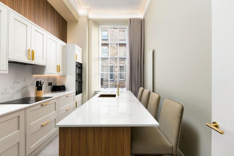 Modern kitchen with white cabinetry, marble countertop, wood-paneled island, and dining seating
