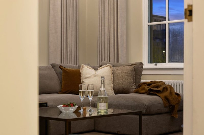 Cozy seating nook with gray sofa, cushions, throw blanket, and window with curtains