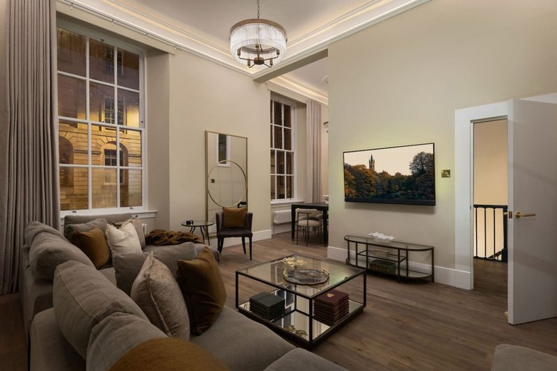 Spacious living room with beige sofa, wooden floors, large windows and framed landscape artwork