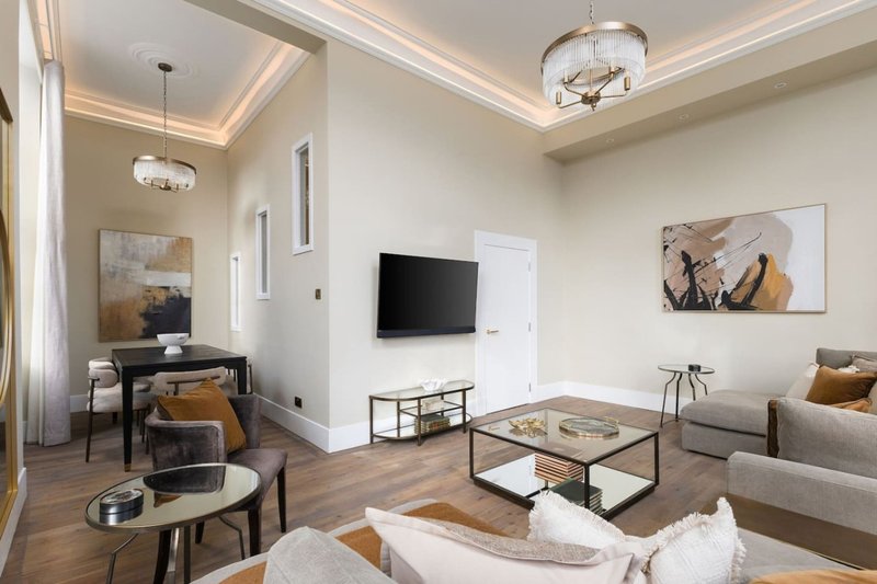 Modern living room with sofa, glass coffee table, wall-mounted TV, and wooden flooring