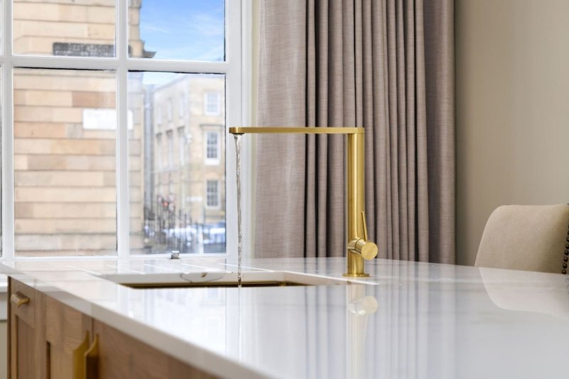 Modern desk workspace with brass lamp, white surface, window view, and grey curtains