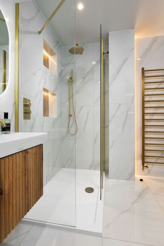 Modern bathroom with marble walls, glass shower enclosure, wooden vanity and heated towel rail