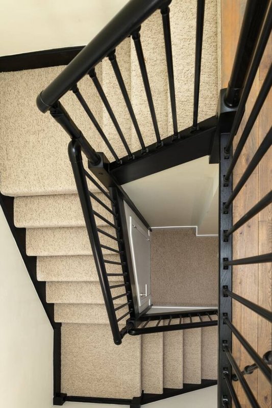 Spiral staircase with black metal railing and carpeted steps viewed from above