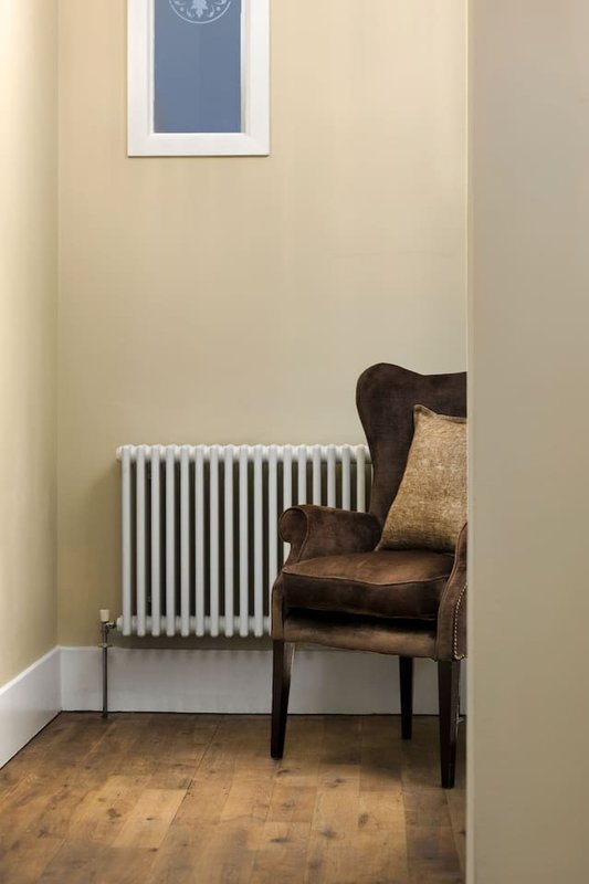 Minimalist corner with brown leather armchair, radiator, and framed window art