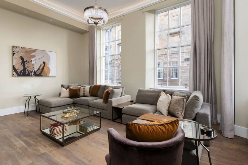 Spacious living room with L-shaped sofa, leather armchair, glass coffee table and large windows