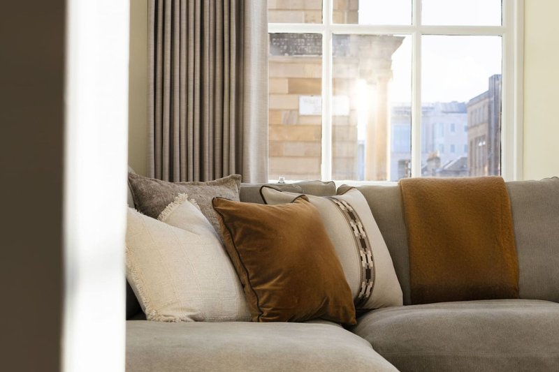 Modern living room with grey sofa, decorative pillows, and large windows overlooking city