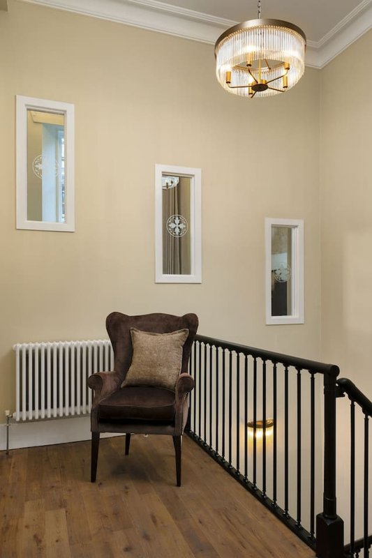 Landing area with black stair railing, brown wingback chair, cream walls and ceiling fixture