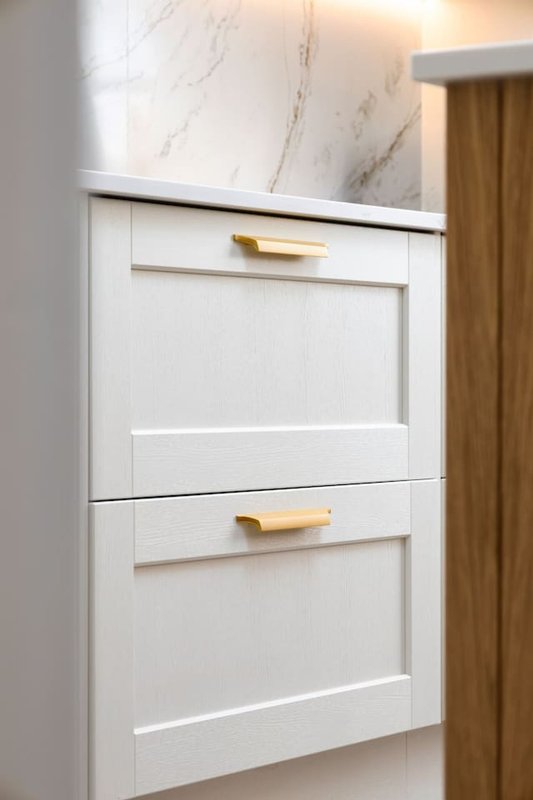 White kitchen cabinetry with brass handles and marble countertop detail