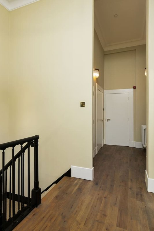 Hallway with wooden flooring, cream walls, white door and black stair railing