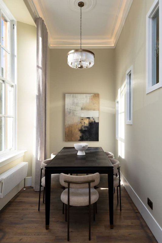 Narrow dining room with black table, chairs, pendant light and framed artwork