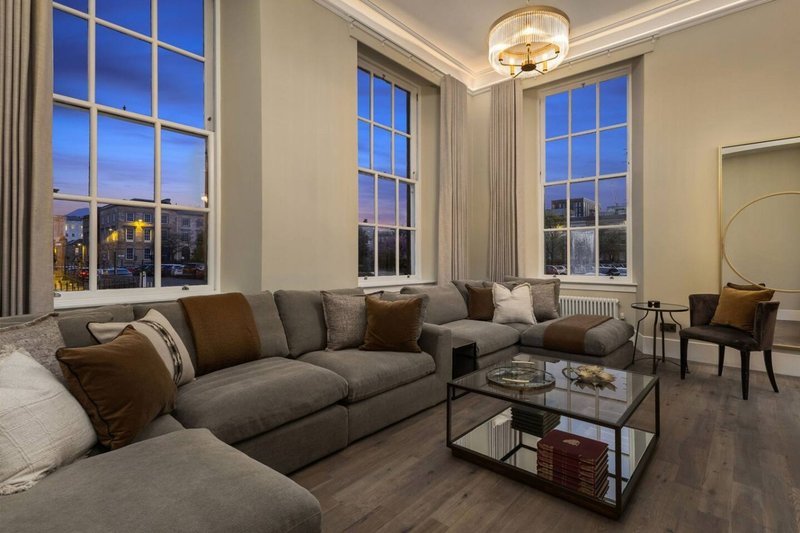 Spacious living room with gray sectional sofa, large windows, and city views at dusk