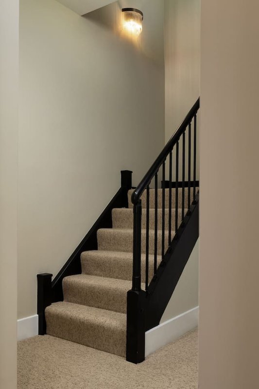 Interior staircase with black metal railings, beige carpet treads and white walls