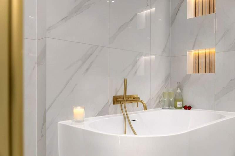 Modern bathroom with white freestanding bathtub, marble tile walls, brass faucet and gold accents