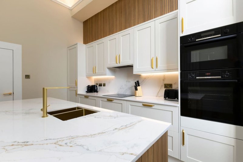 Modern kitchen with white cabinetry, marble countertop, gold handles, and black built-in appliances