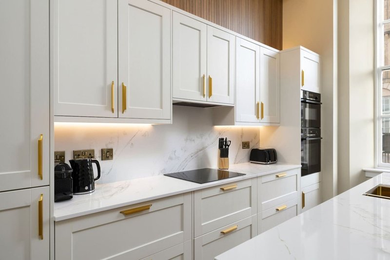 Modern kitchen with white cabinets, marble countertops, gold handles, and integrated appliances