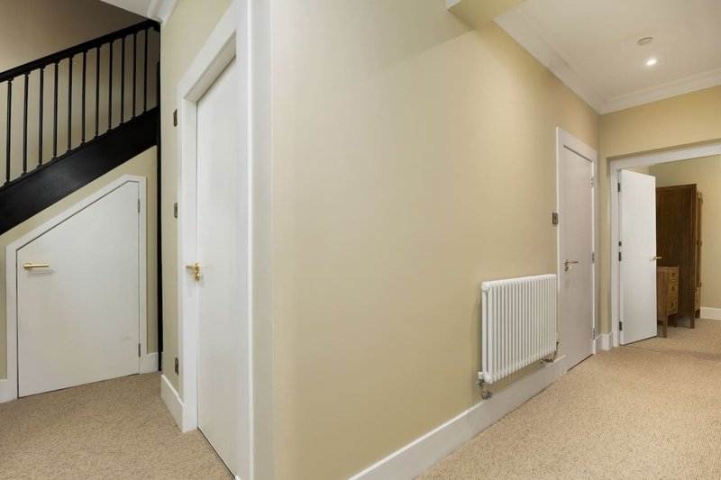 Hallway with cream walls, white doors, radiator, and staircase with black railing