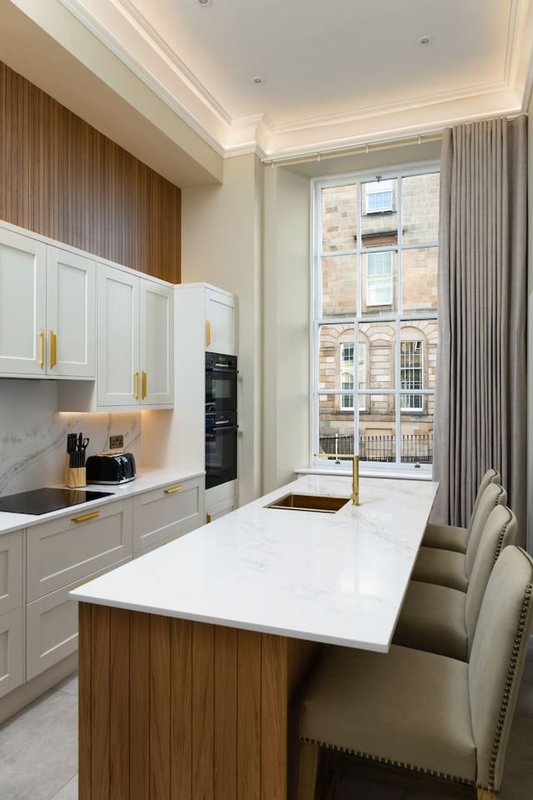Modern kitchen with white cabinetry, wooden accent panels, white countertop island, and city views through glass doors