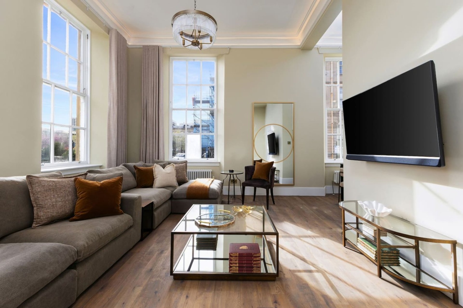 Spacious modern living room with grey sofa, wall-mounted TV, coffee table and city views from windows