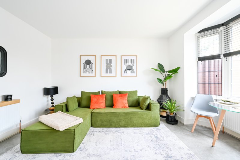 Bright modern living room with green sectional sofa, orange cushions, potted plants and wooden chair