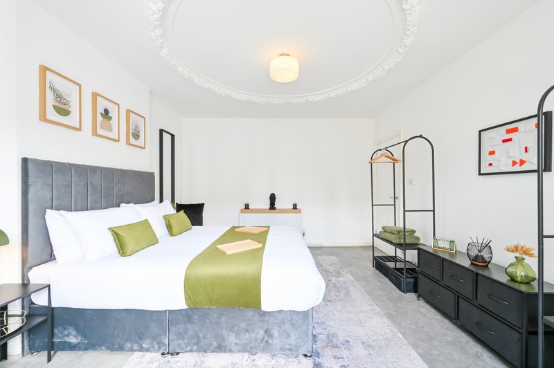 Bedroom with grey upholstered bed, white bedding, green accents, and modern furnishings