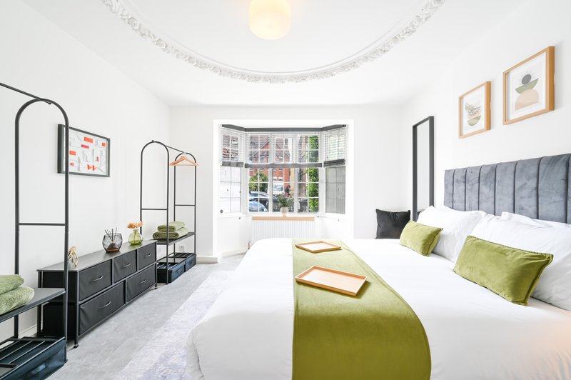 Bright modern bedroom with dual beds, grey upholstered headboard, green cushions and throws