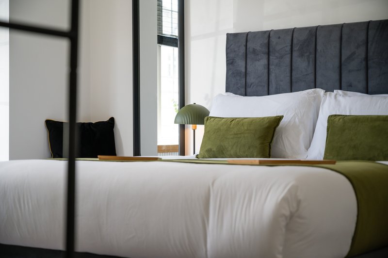 Modern bedroom with dark upholstered headboard, white bedding, olive green cushions and black four-poster frame
