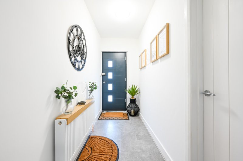 Bright hallway with dark blue front door, wall-mounted clock, potted plants, wooden shelving and framed artwork