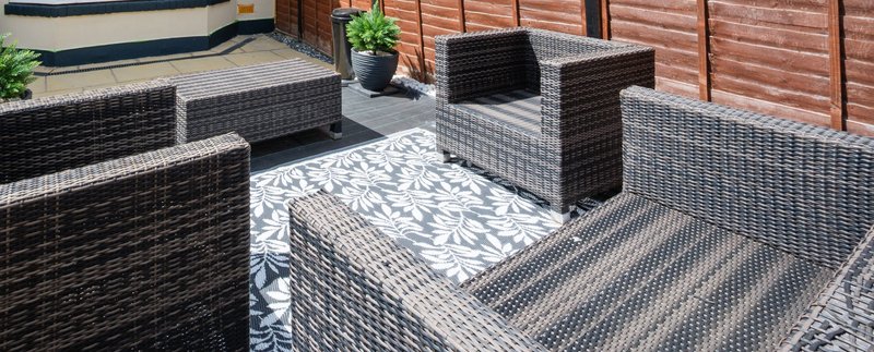 Outdoor patio with rattan furniture, potted plant, and paved flooring