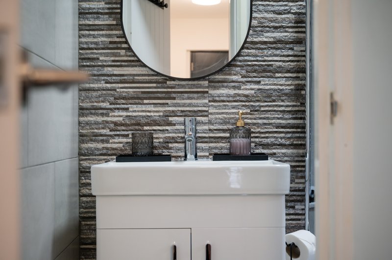 Modern bathroom with white vanity, dual sinks, round mirror and striped tile backsplash