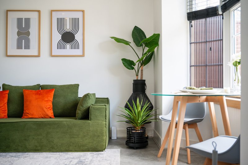 Modern living room with green sofa, orange cushions, potted plants, wooden desk and framed wall art