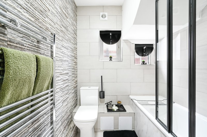 Modern bathroom with white tile walls, heated towel rack, toilet, sink and shower enclosure