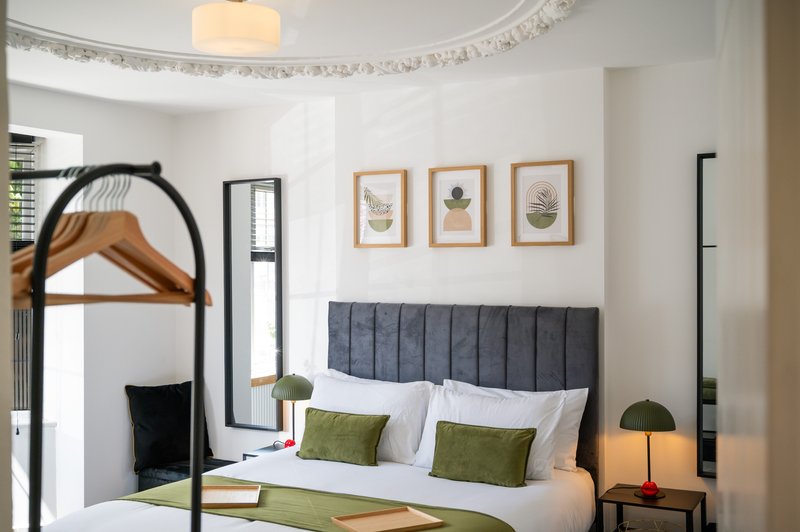 Bedroom with four-poster bed, grey upholstered headboard, botanical wall art, and pendant lighting
