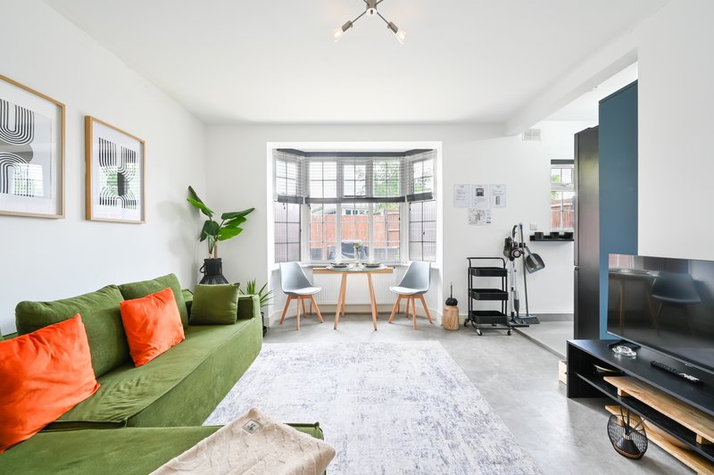 Bright living room with green sofa, orange cushions, bay window, dining area and TV