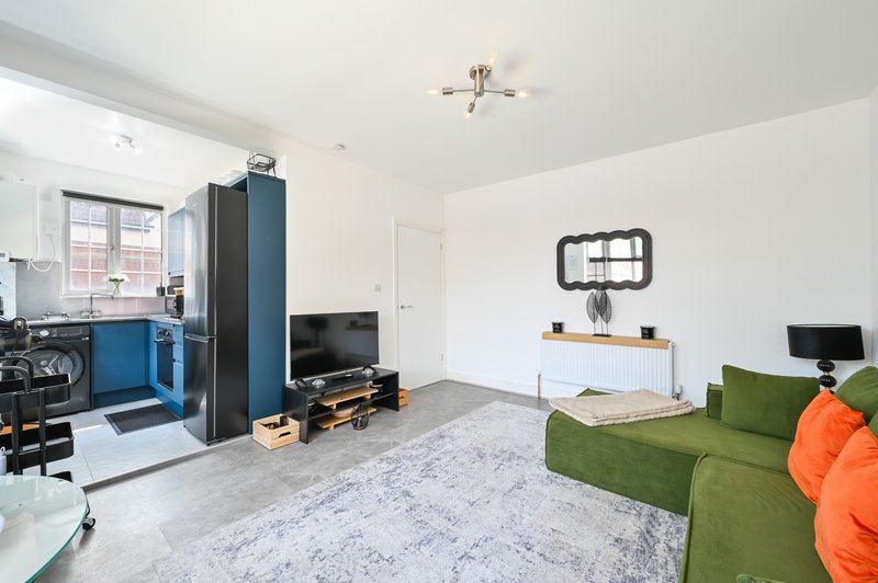 Open-plan living space with green sofa, TV units, kitchen area and ceiling light fixture