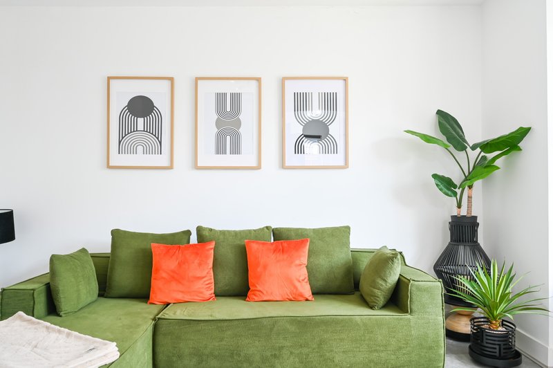 Modern living room with green sofa, orange cushions, framed wall art and potted plants