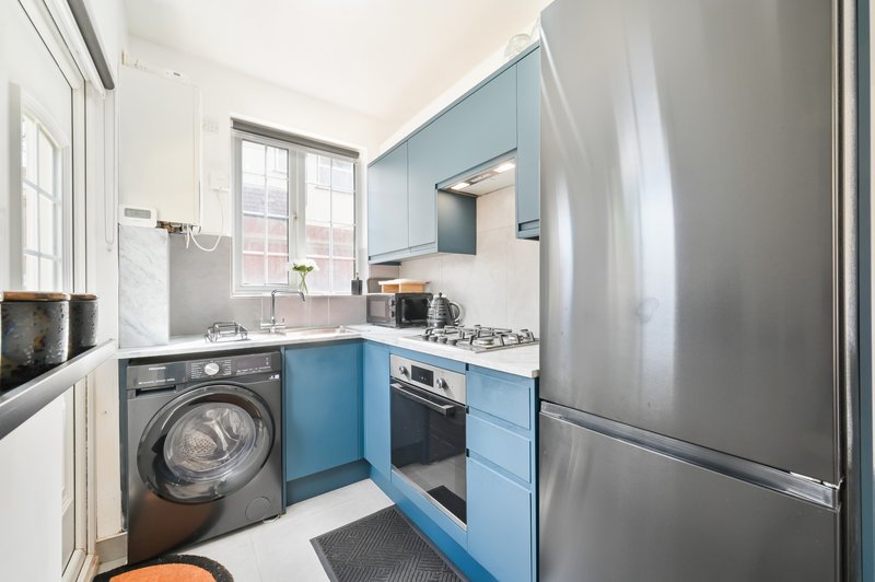 Compact kitchen with blue cabinetry, stainless steel appliances, washing machine and window