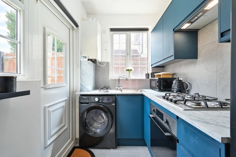 Modern kitchen with blue cabinets, washing machine, gas hob, and window overlooking brick houses