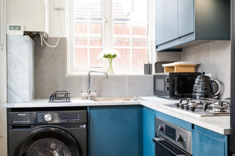 Modern kitchen with blue cabinetry, marble countertop, washing machine and gas hob