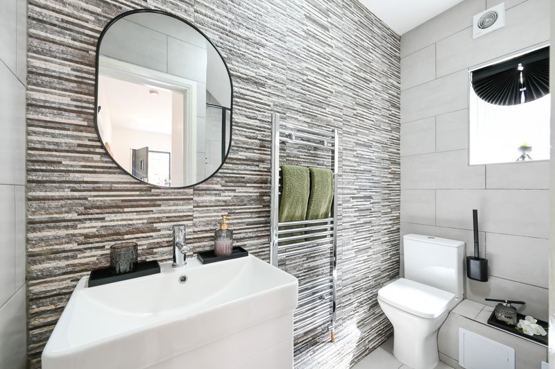Modern bathroom with striped tile walls, white sink, round mirror, heated towel rail and toilet